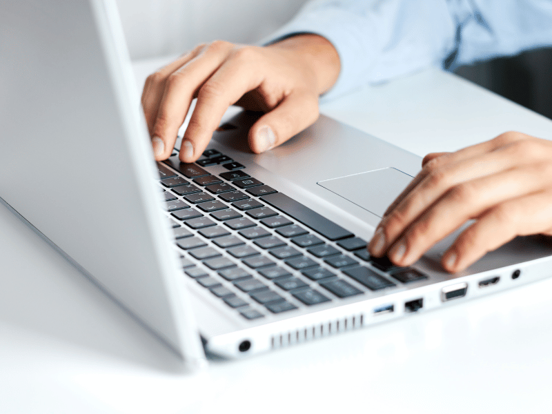 Choosing+website Person typing on a silver laptop keyboard in a bright workspace, focusing on work or study tasks.